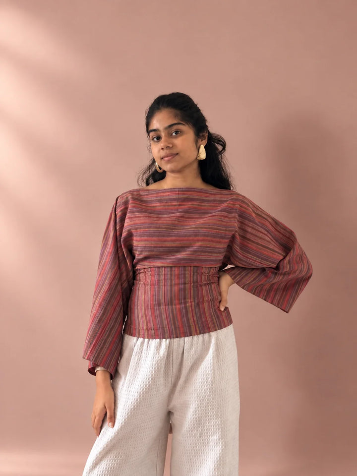Woman in the Rosé Stripe Tie-Back Top, a pink and rust striped bell sleeve top in Indian cotton, worn with white trousers
