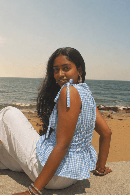 Woman sitting on a beach wearing a blue checkered dress.