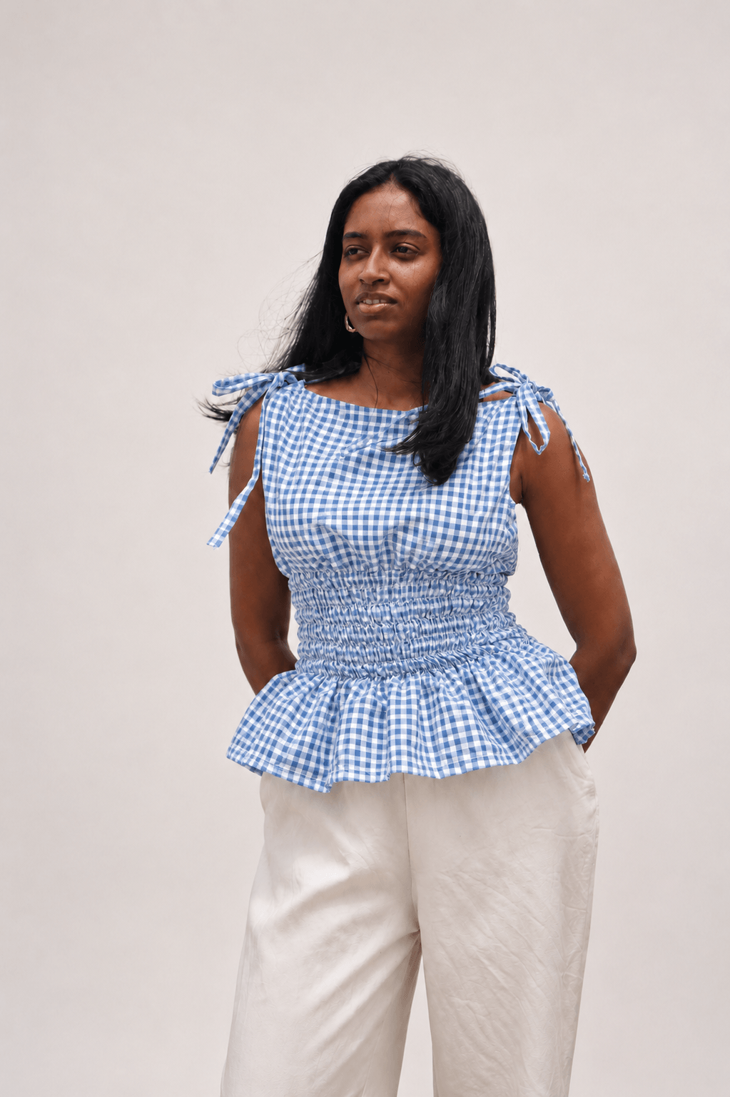 Woman wearing a blue checkered top with tied sleeves against a plain background