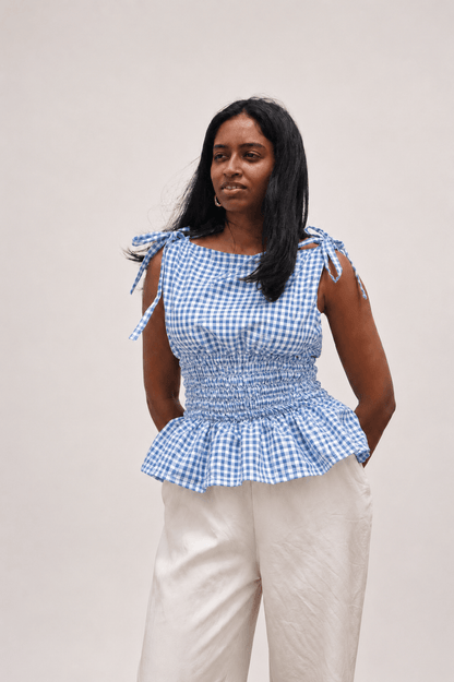 Woman wearing a blue checkered top with tied sleeves against a plain background