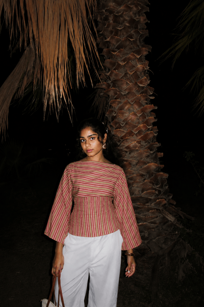 Woman wearing a striped top and white pants standing against a dark background with palm tree.