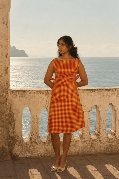 Woman in an orange checkered dress standing on a balcony with ocean view