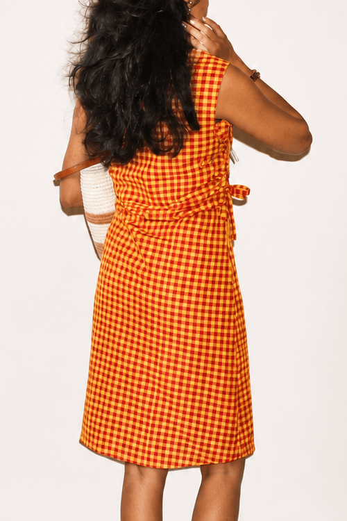 Woman wearing an orange checkered dress with a plain background