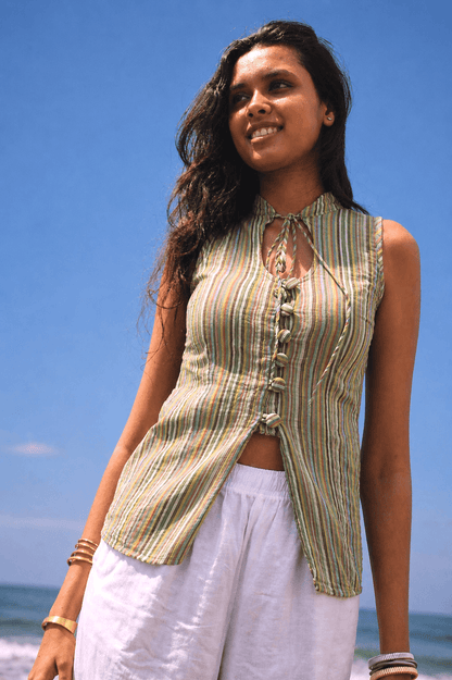 Woman wearing a striped sleeveless top and white pants against a blue sky.