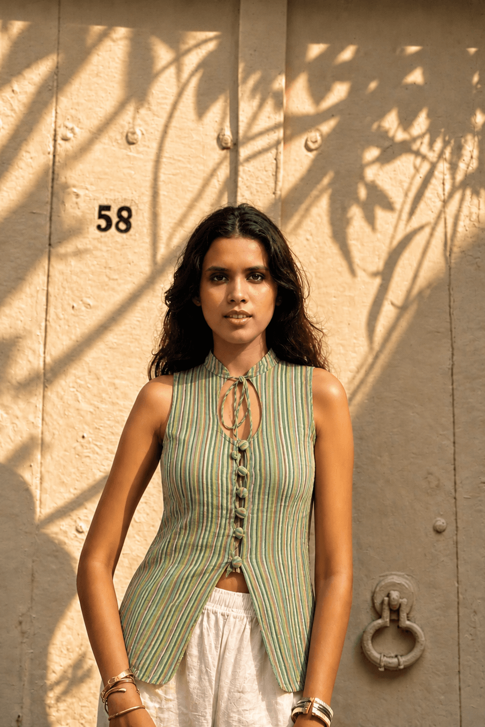 Woman standing against a textured wall with number 58, wearing a green striped sleeveless top.