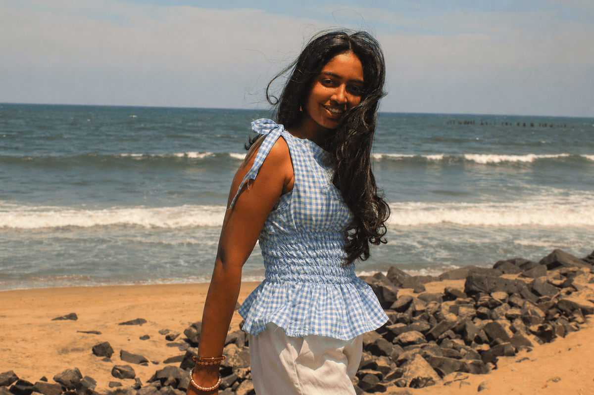 Woman in the Bluebell Breeze gingham top on a beach with the sea behind