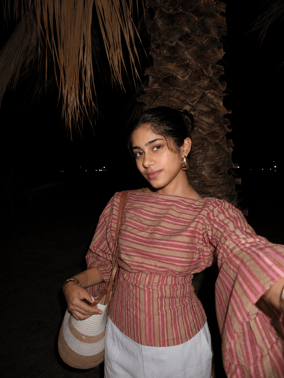 Woman in the Rose Stripe Tie-Back Top with a shoulder bag under palm leaves