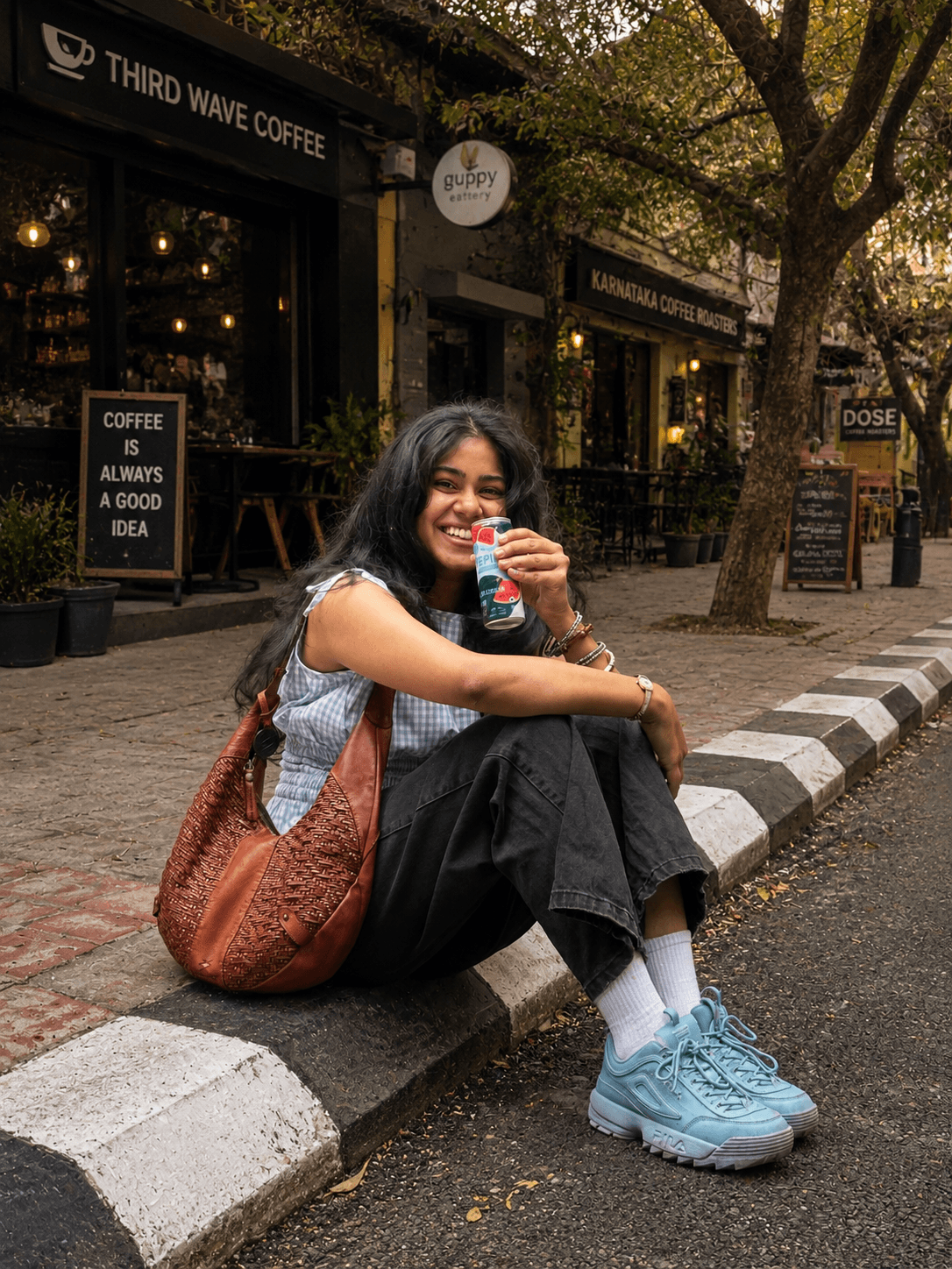 Woman in the Bluebell Breeze gingham top seated on a kerb outside a coffee shop